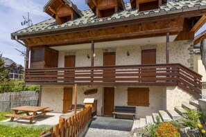 A two-story wooden building with a balcony, a wooden bench, and a picnic table.