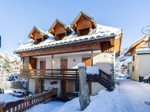 A chalet with a wooden facade, a balcony, and a snow-covered roof.