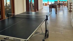 Amplio espacio interior con mesa de ping pong, muebles de madera y vista a la playa.