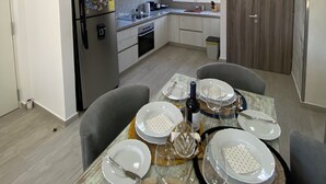 Una cocina moderna equipada con microondas, horno y lavamanos. Hay un comedor con una mesa dispuesta para cuatro personas, incluyendo platos, vasos y cubiertos.