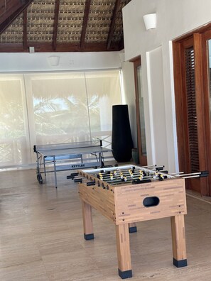 A room with a wooden foosball table, a ping pong table, and a large black speaker.