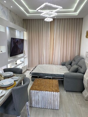 Una camera da letto moderna con un letto, un divano grigio, un tavolo da pranzo e una TV montata a parete.