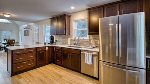 A modern kitchen with dark wood cabinets, stainless steel appliances, and a large island with a sink. - Spacious Yard & Deck - Hot Tub - 120” Projector - 12mins-Waterville Valley (Thornton)