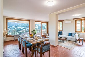 A dining area with a table set for four, large windows, a balcony, and a living room with a sofa.