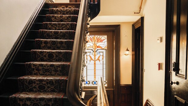 A staircase with patterned carpet, a metal handrail, and a wooden floor leading to a door with a stained glass window. - Rome Room - Villagio Boutique Hotel ★WALK to STADIUM ★FREE PARKING (Pittsburgh)