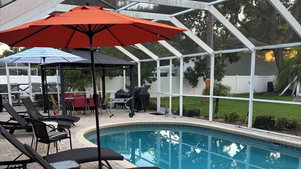 A pool area with lounge chairs and umbrellas, surrounded by a covered patio. - Charming studio in beautiful Palm Harbor with A/C, Swimming Pool and Patio (Palm Harbor)