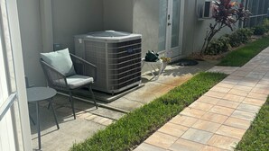 A residential exterior with a patio, outdoor furniture, an air conditioning unit, and a small garden. - Charming studio in beautiful Palm Harbor with A/C, Swimming Pool and Patio (Palm Harbor)