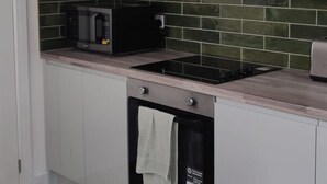 Uma cozinha com armários brancos, micro-ondas preto, exaustor de aço inoxidável e painel de azulejos verdes.