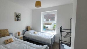 Quarto com duas camas, janela com vista, abajur e prateleira na parede.