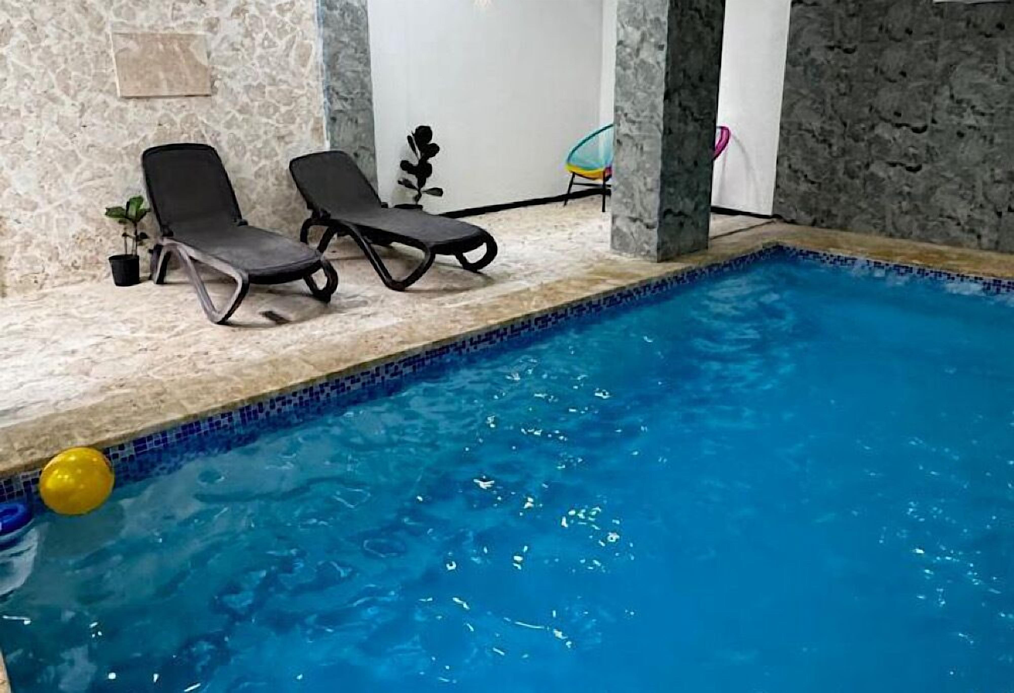 An indoor swimming pool with two lounge chairs and a potted plant.