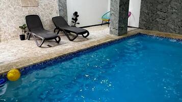 An indoor swimming pool with two lounge chairs and a potted plant.