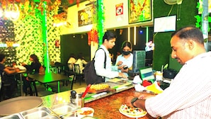 A restaurant interior with tables, chairs, and a counter where food is being prepared. - Hotel Ambassador Grand (Varanasi)