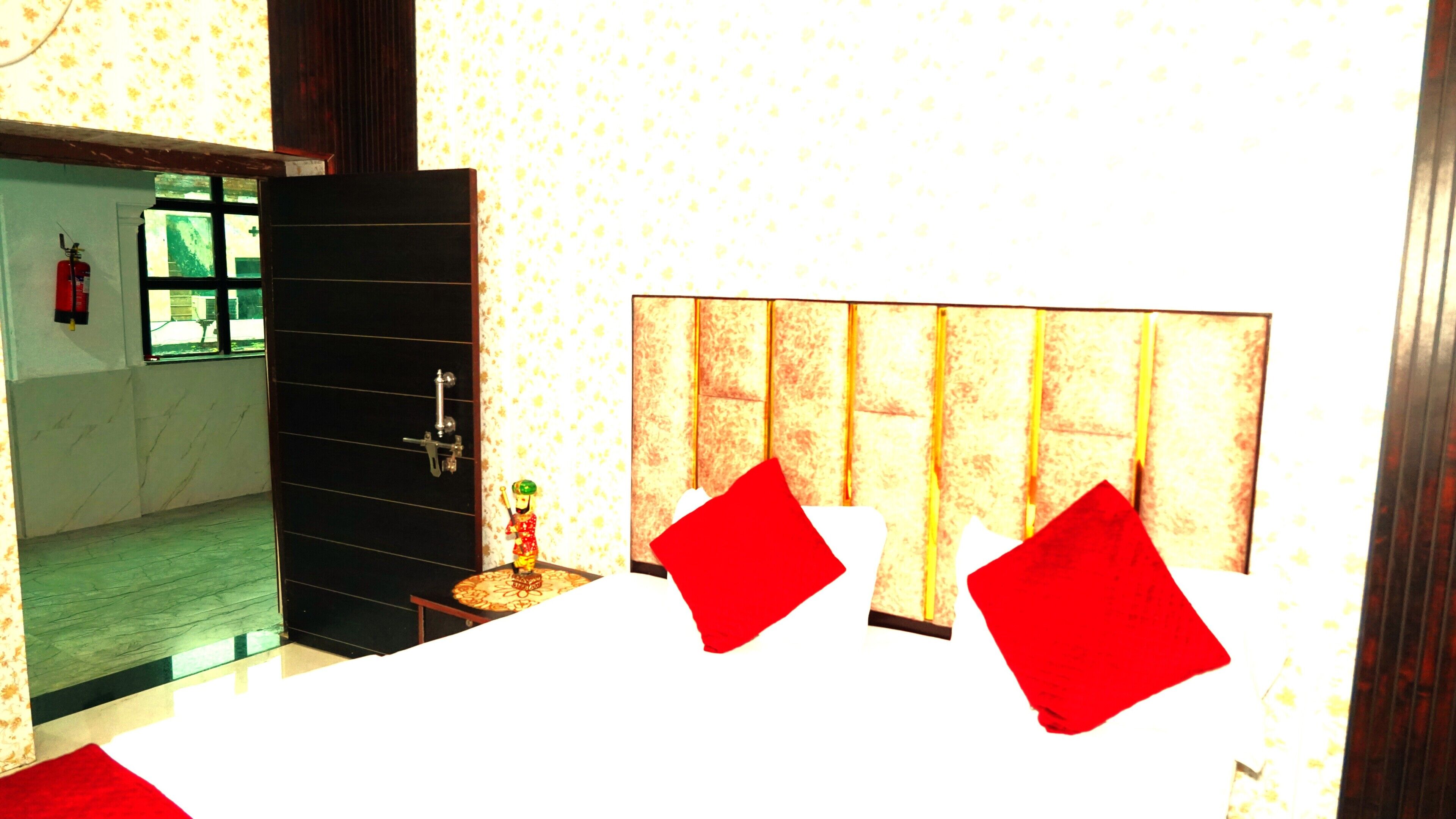 A hotel room with a large window, a door, and a bed with a red pillow.