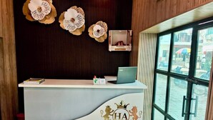 A reception desk with a laptop, a book, and a small decorative item. The desk has a logo with "HA" and "HOTEL AMBASSADOR GRAND" written on it. - Hotel Ambassador Grand (Varanasi)