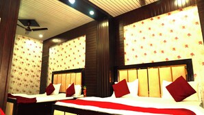 A hotel room with two beds, wooden headboards, floral wallpaper, and a ceiling fan. - Hotel Ambassador Grand (Varanasi)