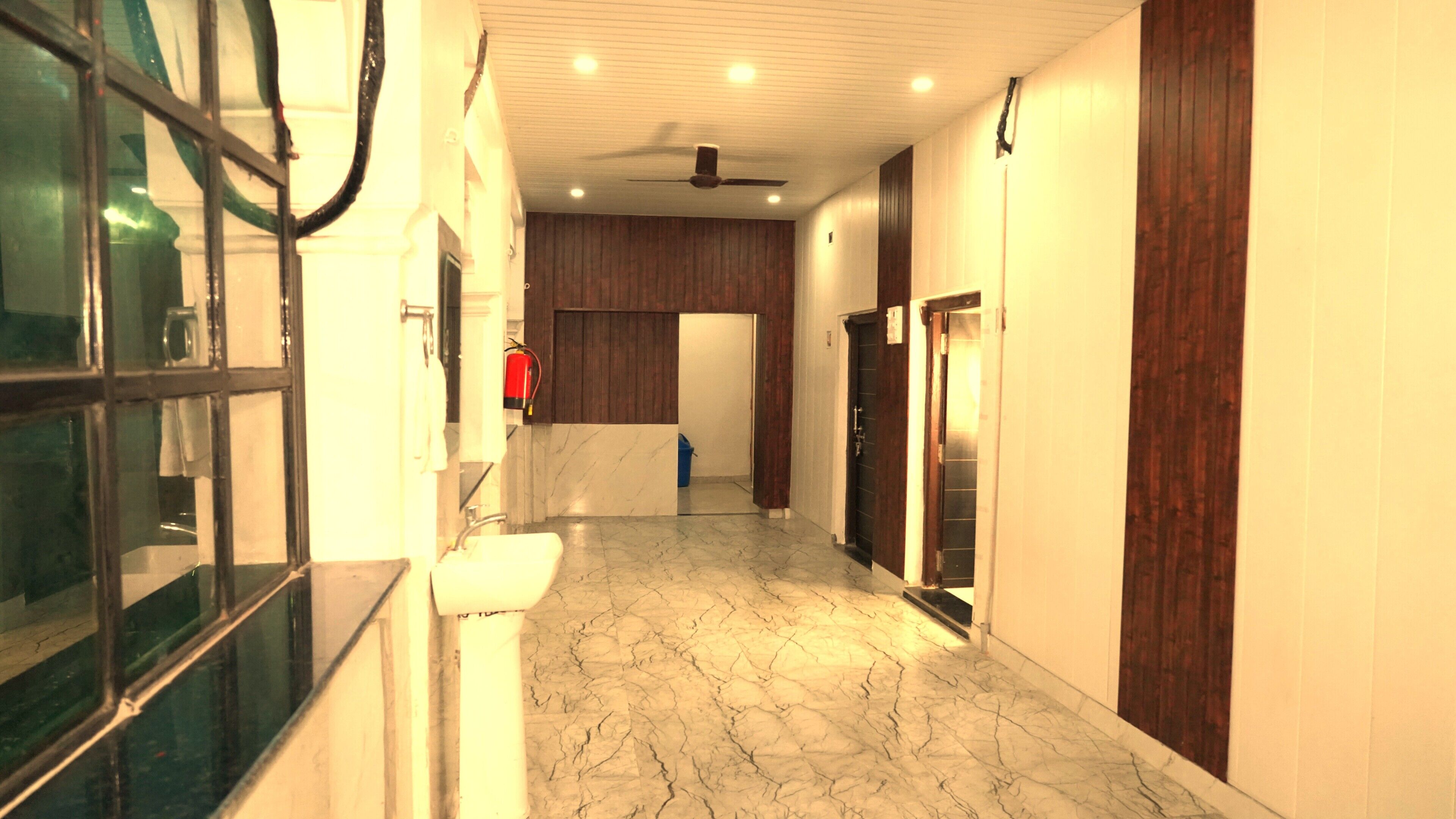A hallway with a marble floor, wooden paneling, a ceiling fan, and a fire extinguisher.