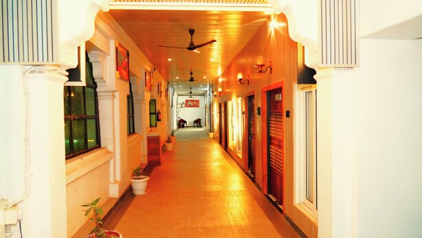 A corridor with a ceiling fan, potted plants, and doors on both sides. - Hotel Ambassador Grand (Varanasi)