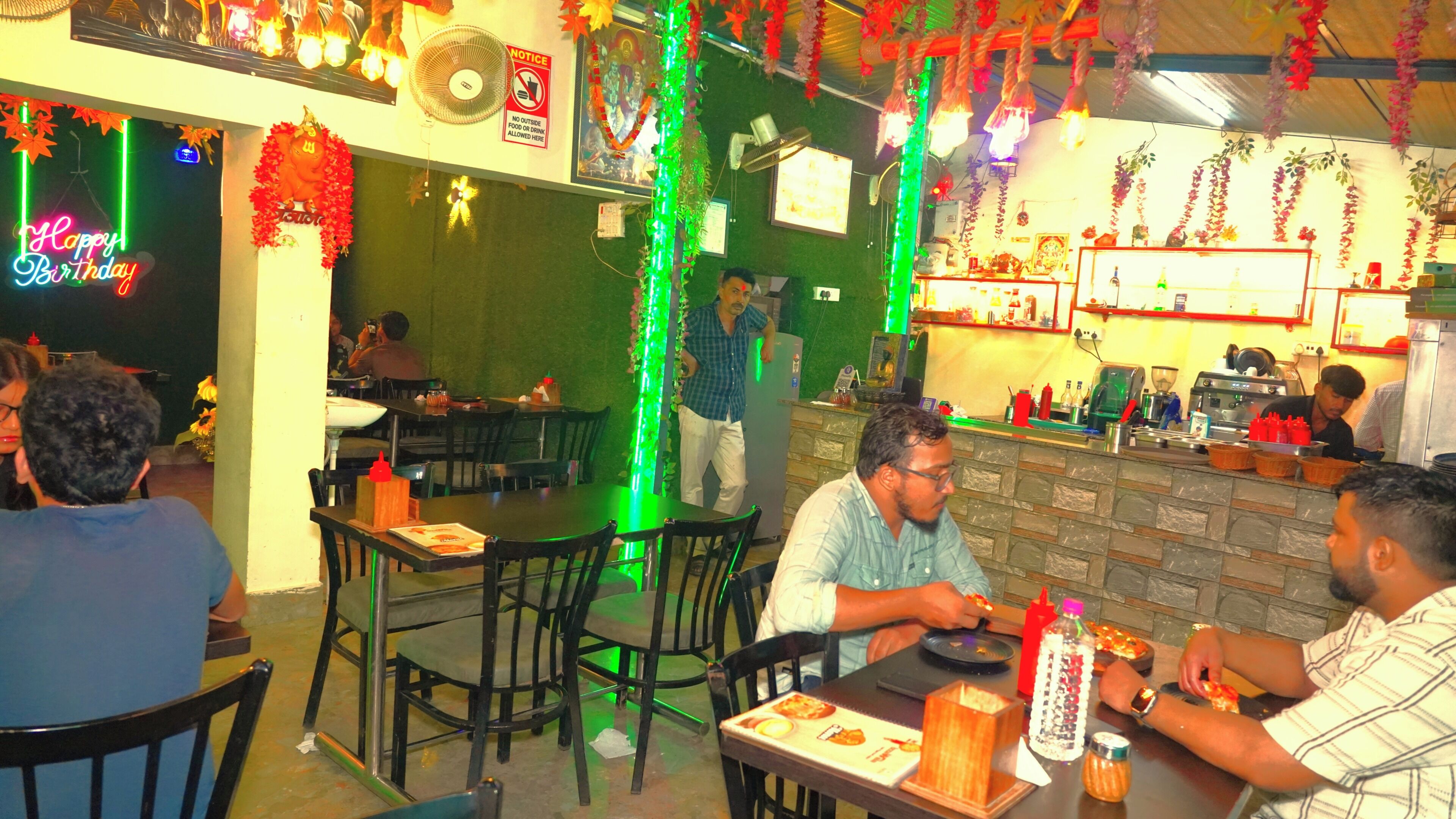 A restaurant with tables and chairs, a counter with kitchen equipment, and a neon sign.