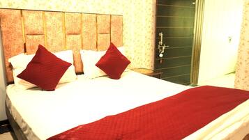 Habitación de hotel con una cama grande, dos almohadas rojas, una colcha blanca y una manta roja.
