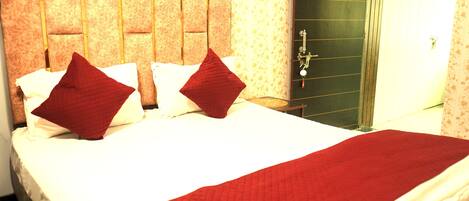 Une chambre d’hôtel avec un grand lit, deux oreillers rouges, un couvre-lit blanc et une couverture rouge.