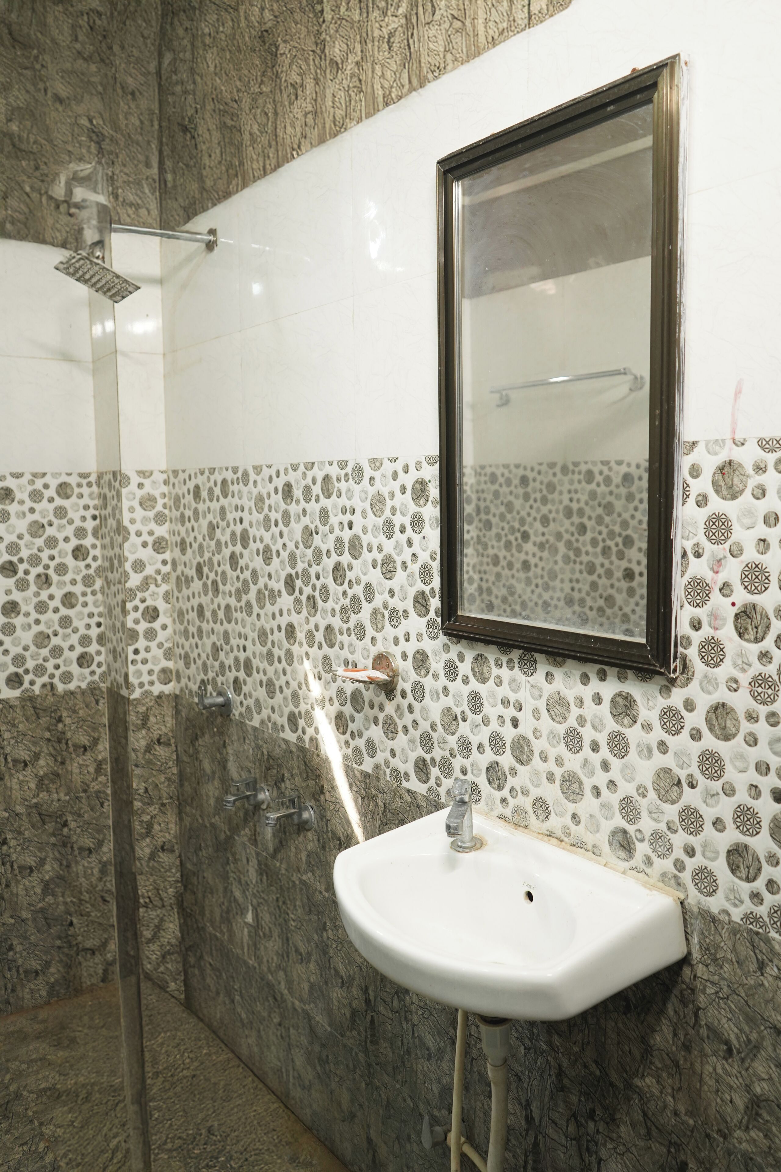 A bathroom with a glass shower enclosure, a white sink, and patterned tile walls.