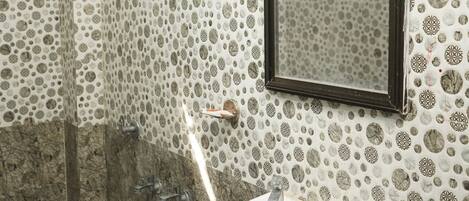 A bathroom with a glass shower enclosure, a white sink, and patterned tile walls.