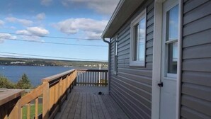 Eine Holzterrasse mit Seeblick, ein Haus mit weißer Tür und einem Geländer.