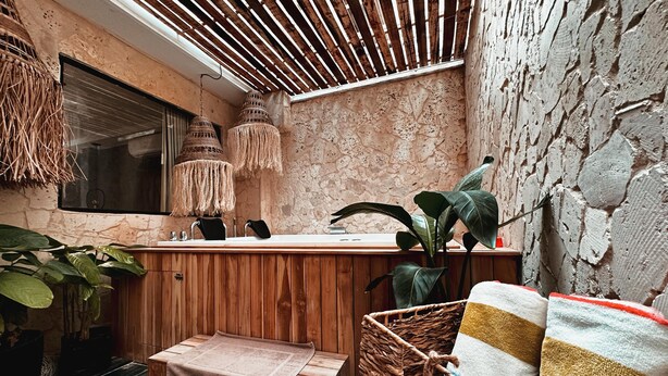 A cozy bathroom with a wooden vanity, a stone wall, a hanging light, and a potted plant. - Vacation Home (For Friends and Family) (Medellín)