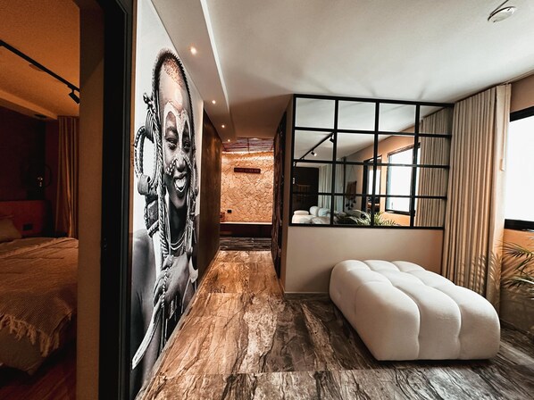 A modern hotel room with a large mirror, a plush ottoman, and a mural on the wall.