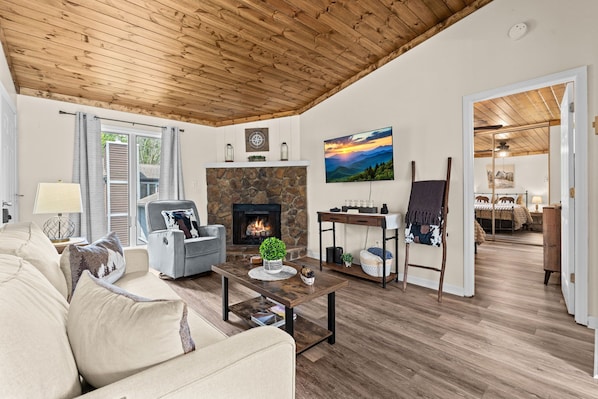 A cozy living room with a fireplace, a sofa, a coffee table, and a painting on the wall.
