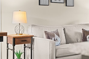 Un salon avec un canapé, une table d’appoint sur laquelle se trouve une lampe, et un tableau encadré accroché au mur.