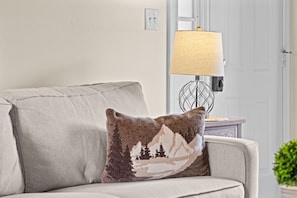 Ein Wohnzimmer mit einer Couch, einem Zierkissen, einer Lampe und einer Tür.