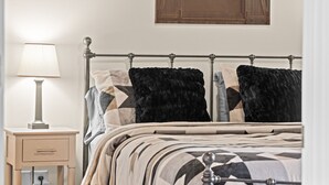 Un dormitorio con estructura de cama metálica, una mesita de noche con lámpara y un armario de madera sobre la cama.
