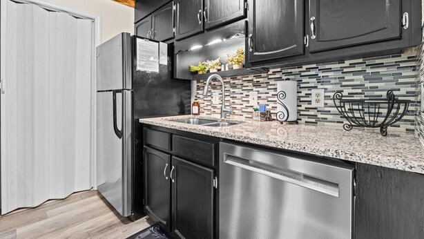 Una cocina con armarios oscuros, un refrigerador de acero inoxidable, encimera de granito y salpicadero de azulejos.