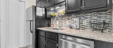 A kitchen with dark cabinets, a stainless steel refrigerator, a granite countertop, and a tiled backsplash.
