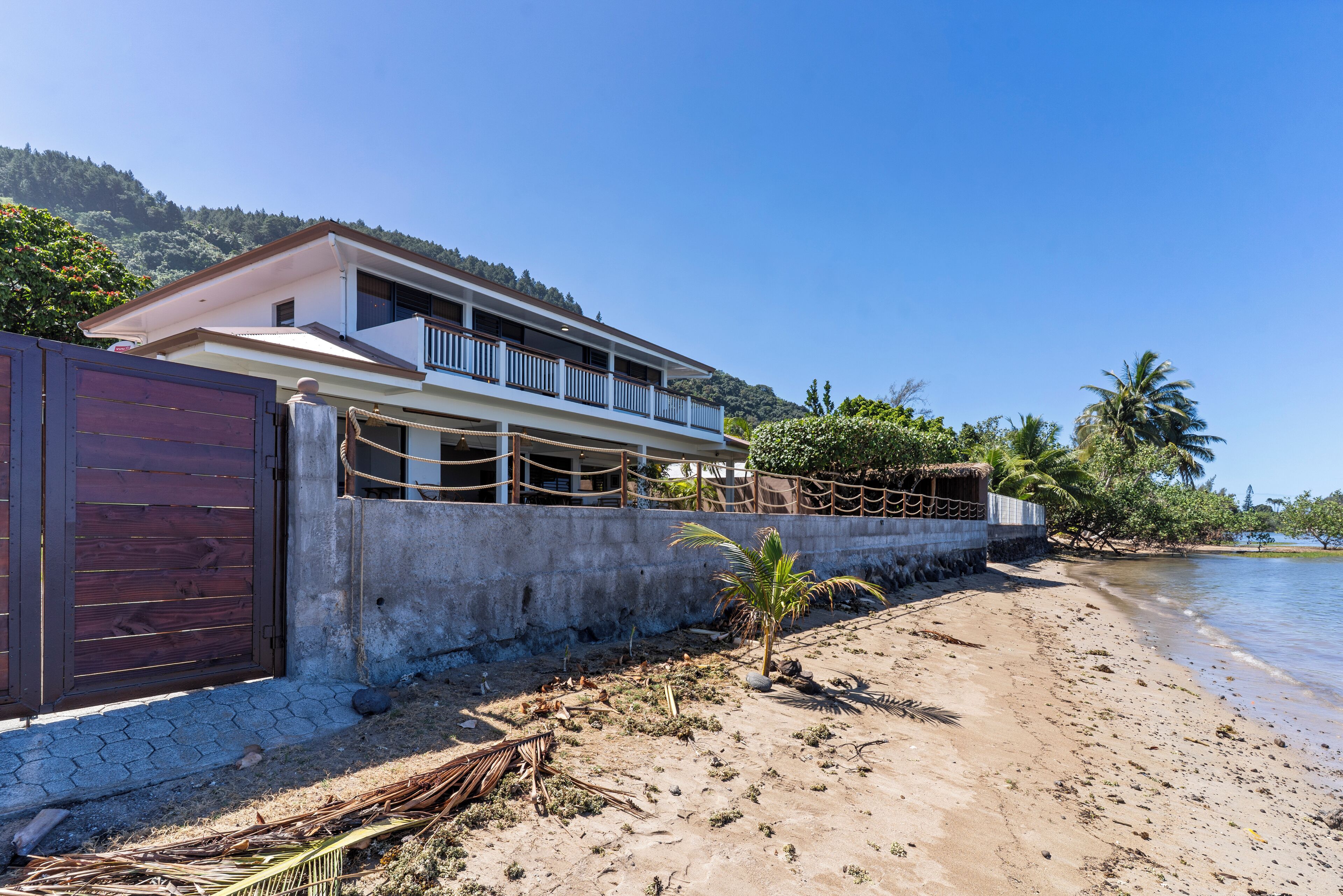 A beachfront property with a two-story building, a concrete wall, and a palm tree.