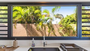 A kitchen with a large window overlooking a tropical garden. - Hinarani Villa (Paea)