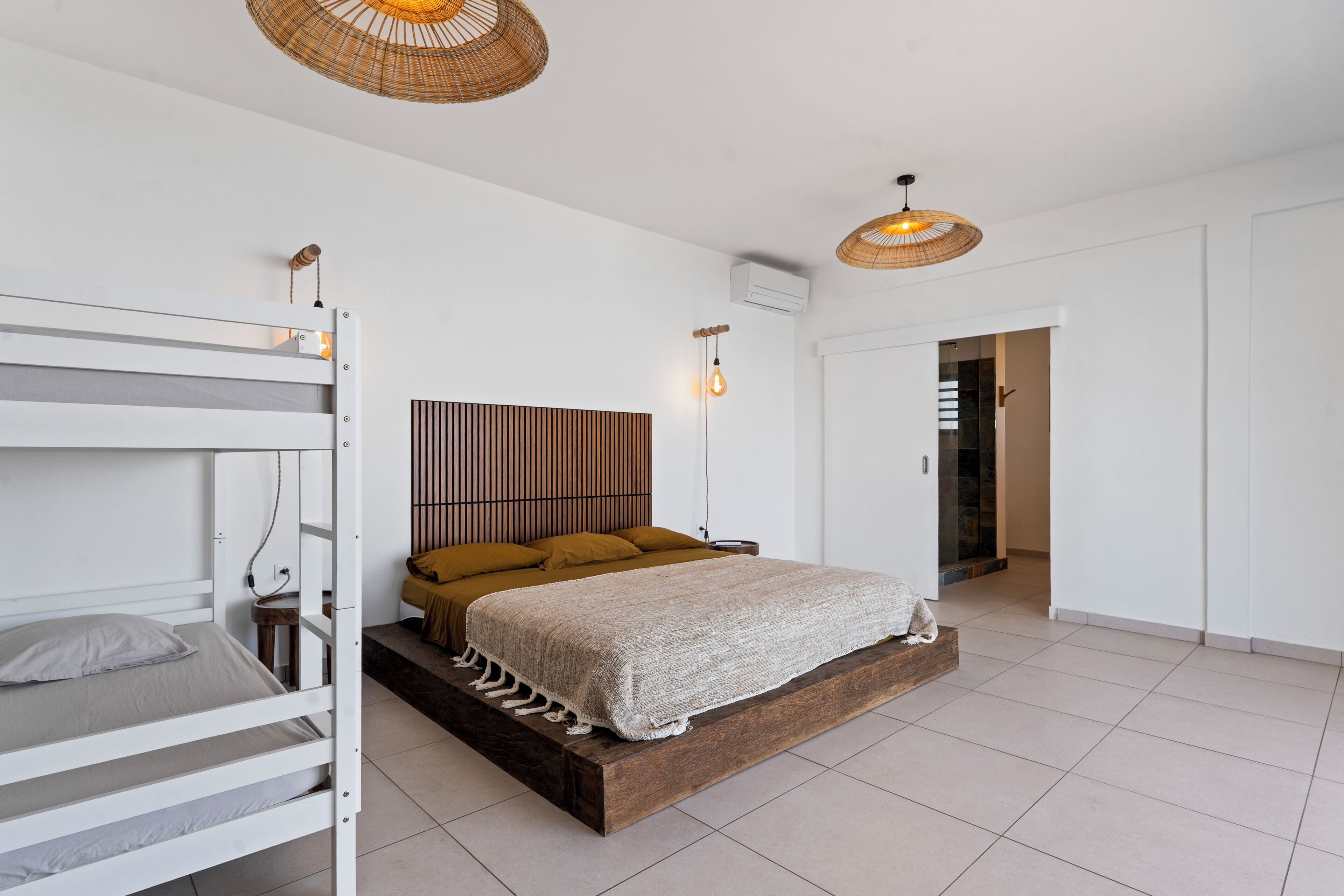 A bedroom with a bunk bed, a wooden platform bed, a headboard, and two pendant lights.