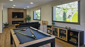 A modern living room with a pool table, a flat-screen TV mounted on the wall, and a bookshelf filled with board games. - Rural lodging with swimming pool in front of the Cueva del Gato, 9 km from Ronda. (Benaoján(Málaga))