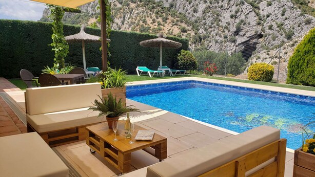 A pool area with lounge chairs, a table with a glass, and a potted plant. - Rural lodging with swimming pool in front of the Cueva del Gato, 9 km from Ronda. (Benaoján(Málaga))