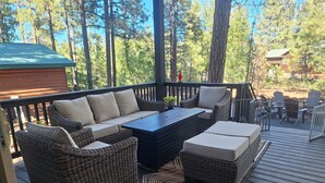 A covered outdoor deck with wicker furniture, a coffee table, and a view of the surrounding forest. - Beautiful 3-bedroom cabin in welcoming Pinetop Country Club (Pinetop Country Club)
