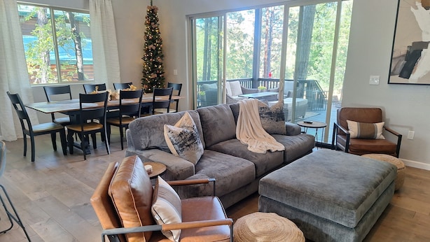 A modern living room with a sectional sofa, a leather armchair, and a coffee table. There is a Christmas tree in the corner, and large windows provide a view of the outdoors. - Beautiful 3-bedroom cabin in welcoming Pinetop Country Club (Pinetop Country Club)