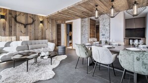 Un salon moderne avec un canapé gris, un coin repas avec une table dressée pour quatre personnes et une cuisine dotée d’un grand îlot central.