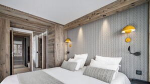 Une chambre moderne avec un plafond en bois, un grand lit avec une literie blanche et deux lampes fixées au mur.