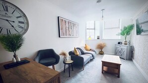 Una sala de estar moderna con un reloj de pared grande, un sofá, una mesa de centro y una mesita auxiliar con adornos.