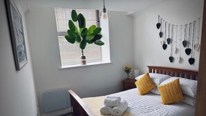 Un dormitorio con una cama de madera, ropa de cama blanca, un plaid amarillo y una planta en maceta junto a la ventana.