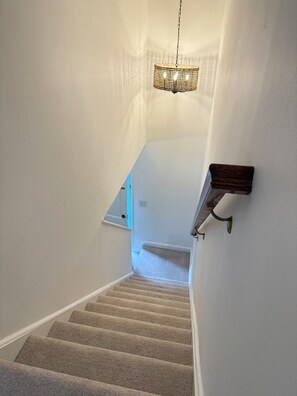 A staircase with carpeted steps leading to a landing, a wall-mounted light fixture, and a small shelf. - Enjoyable townhome  (Alexandria)