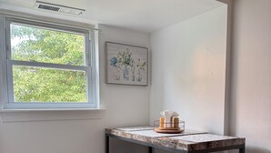 Eine kleine Küche mit Fenster, einem Mülleimer und einem gerahmten Bild an der Wand.