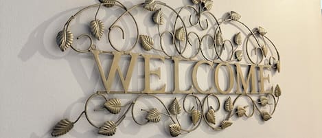 A wall-mounted decorative sign with the word 'WELCOME' in large letters, surrounded by a metal vine design.