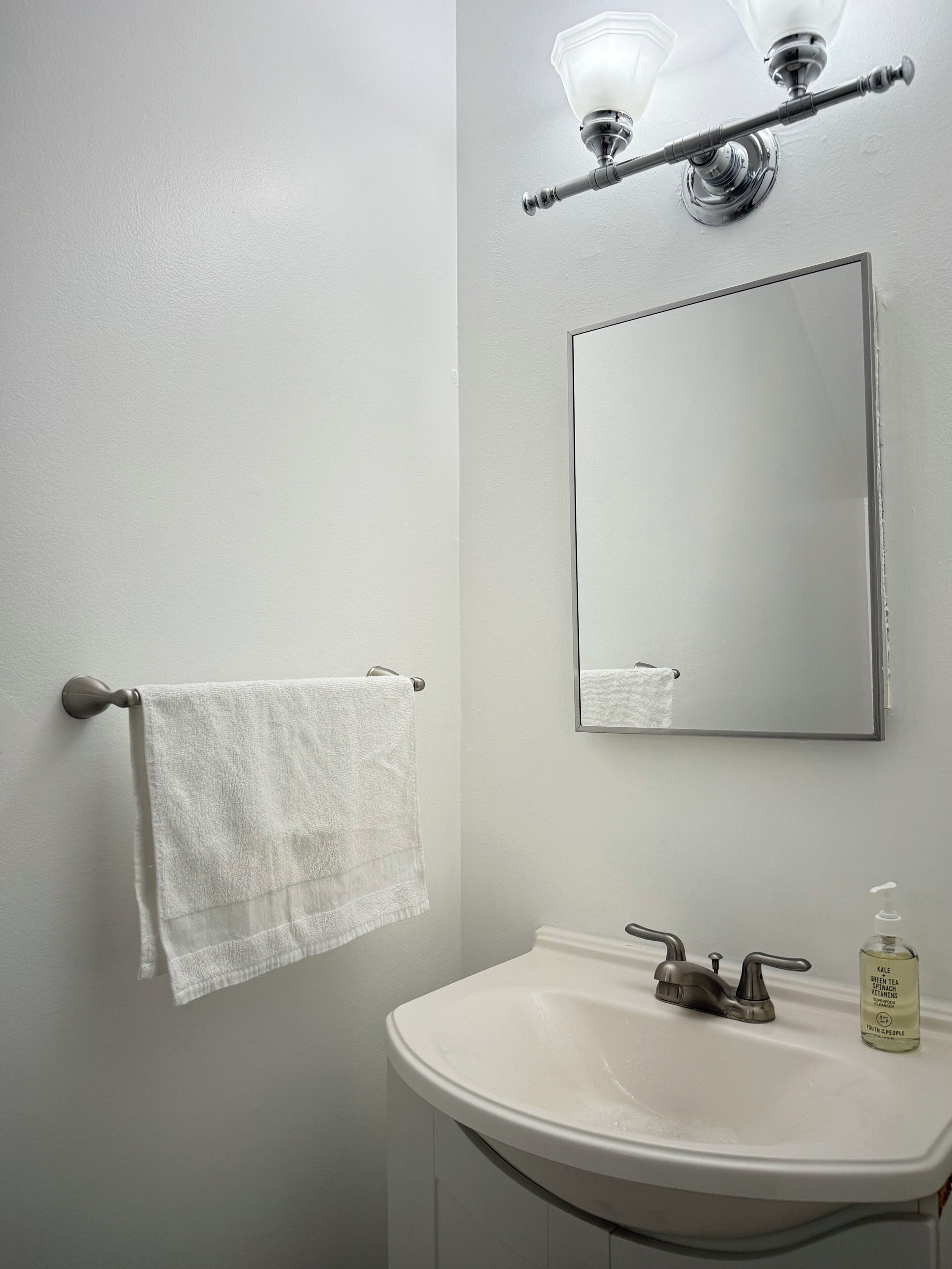 A bathroom with a white sink, a mirror, and a towel hanging on a door.